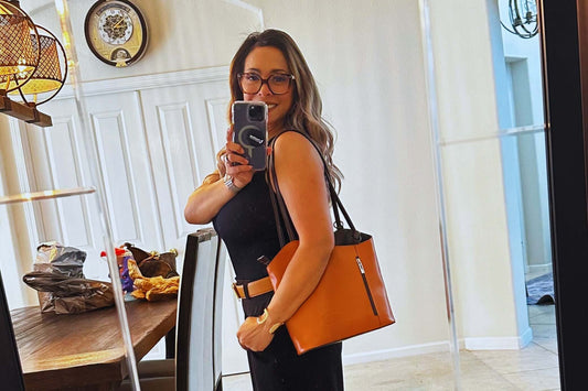 Woman taking a selfie in a mirror, showcasing a stylish orange handbag and a black outfit.